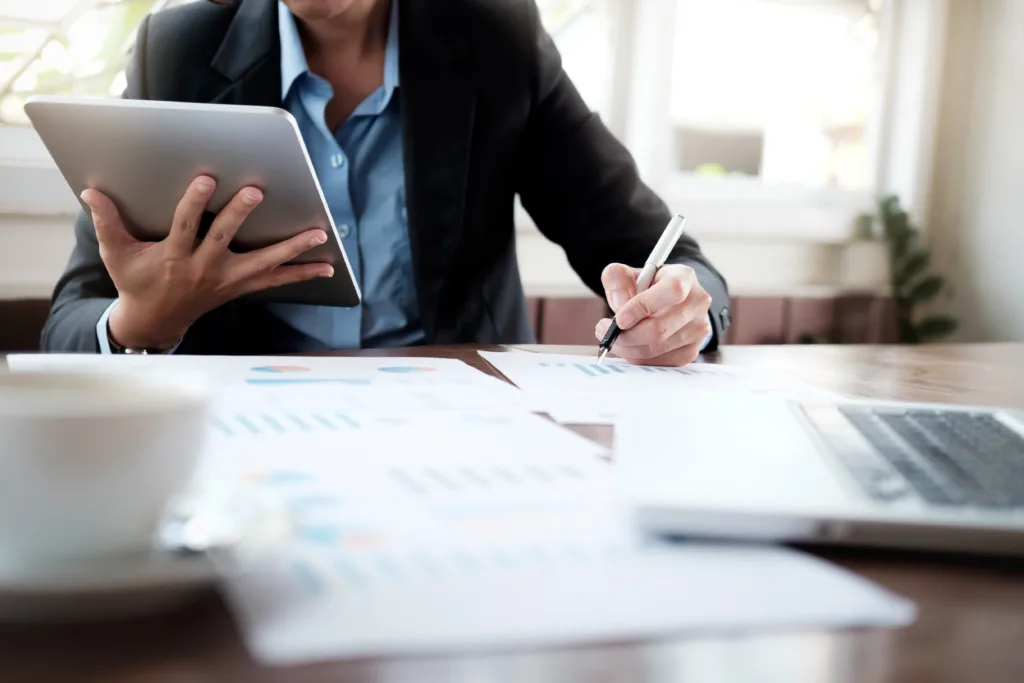 Homem trabalhando com tablet na mão, escrevendo algo em folhas com gráficos.